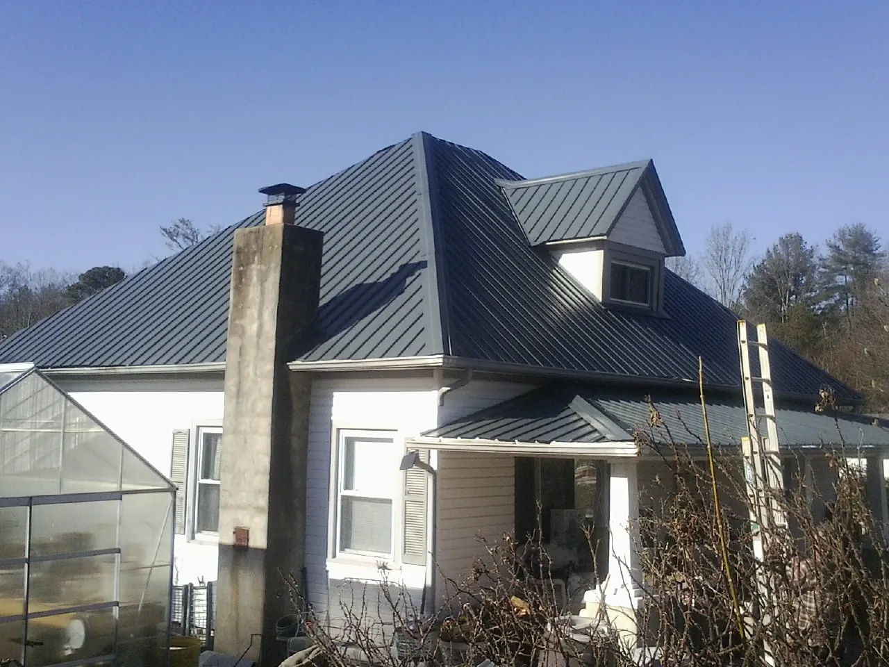 Dark blue standing seam metal roof on a white farmhouse with dormer — Slate & Tile Roof Repair by Roofing Brothers in Tracy City