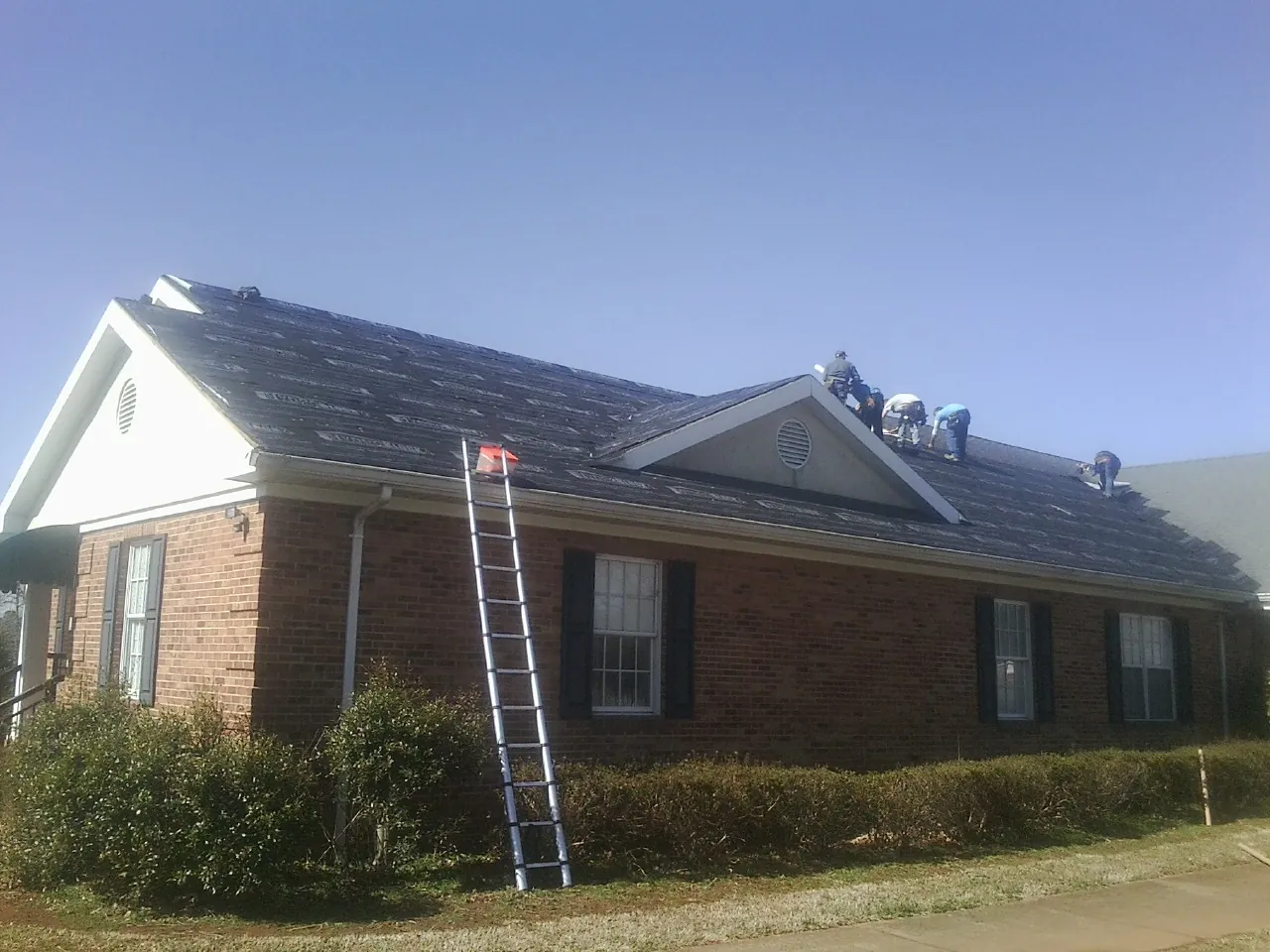 Crew tearing shingles off a brick ranch roof with a ladder set — Metal Roof Repair work by our crew in Tracy City