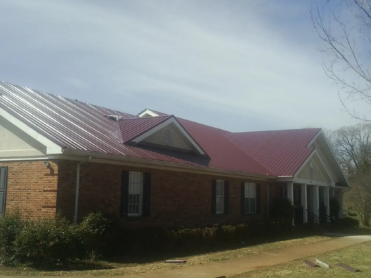 Red metal roof with gabled entries on a long brick building, from a Hail Damage Roof Repair job in Tracy City