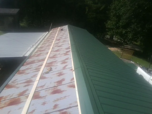 Old rusted panels beside newly installed green metal roofing — Wind Damage Roof Repair by Roofing Brothers in Tracy City