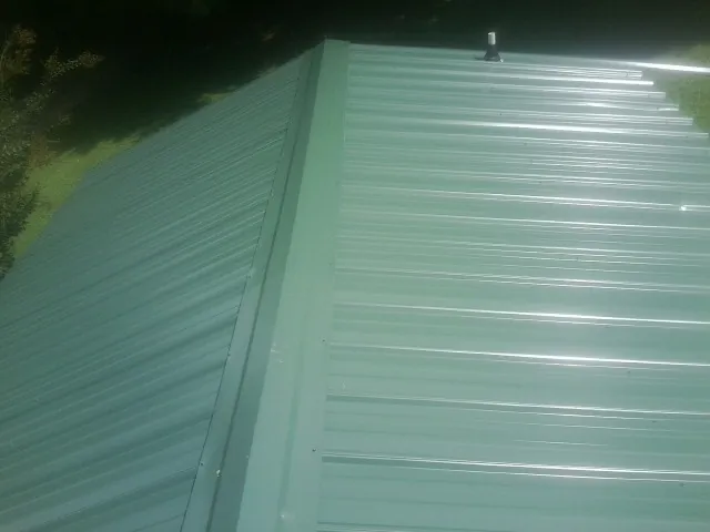 New green metal panels meeting at the ridge of a roof — Flat Roof Repair work by our crew in Tracy City