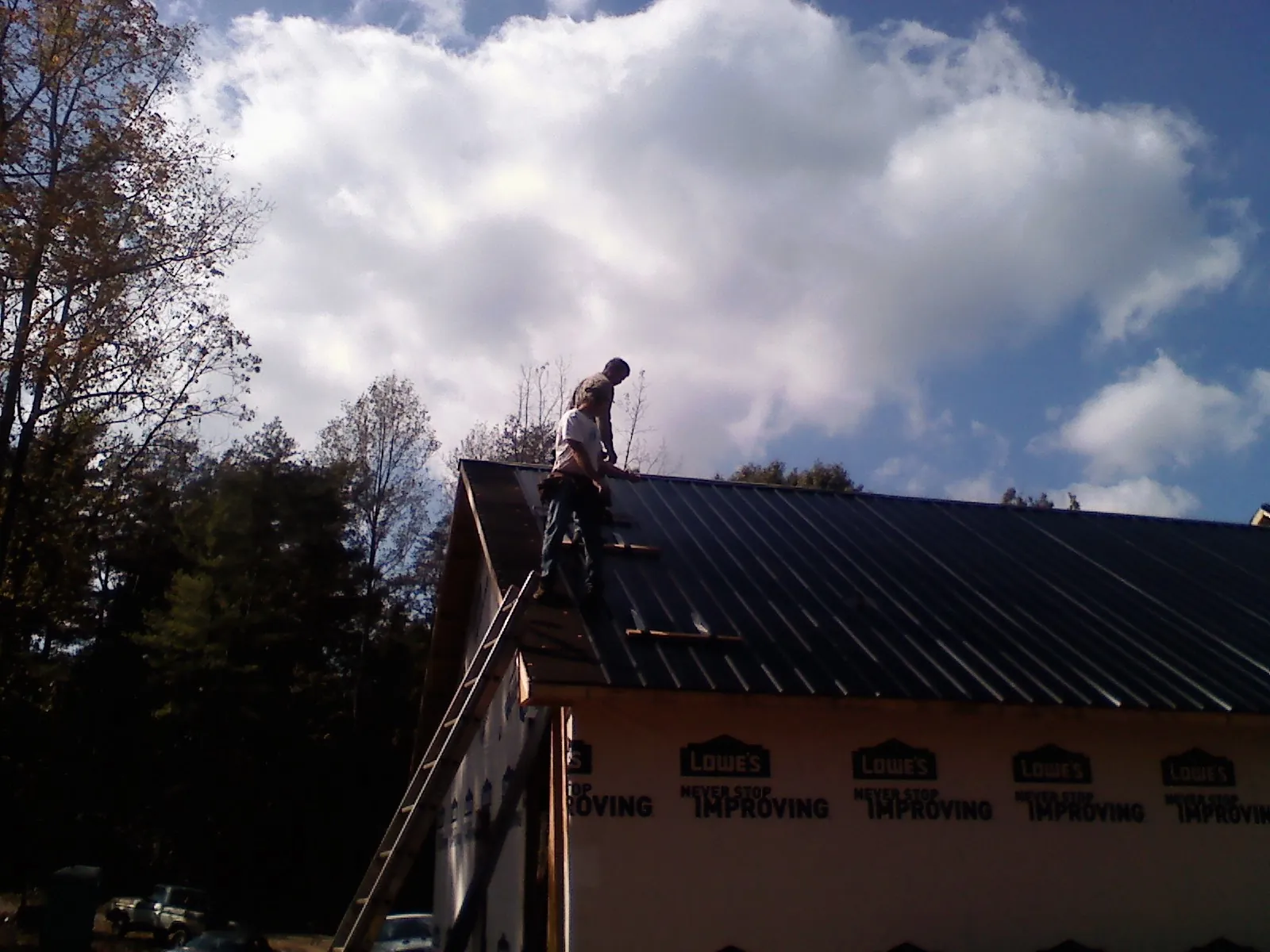 Roofer fastening dark metal panels high against a cloudy sky, from a Roof Inspection job in Tracy City