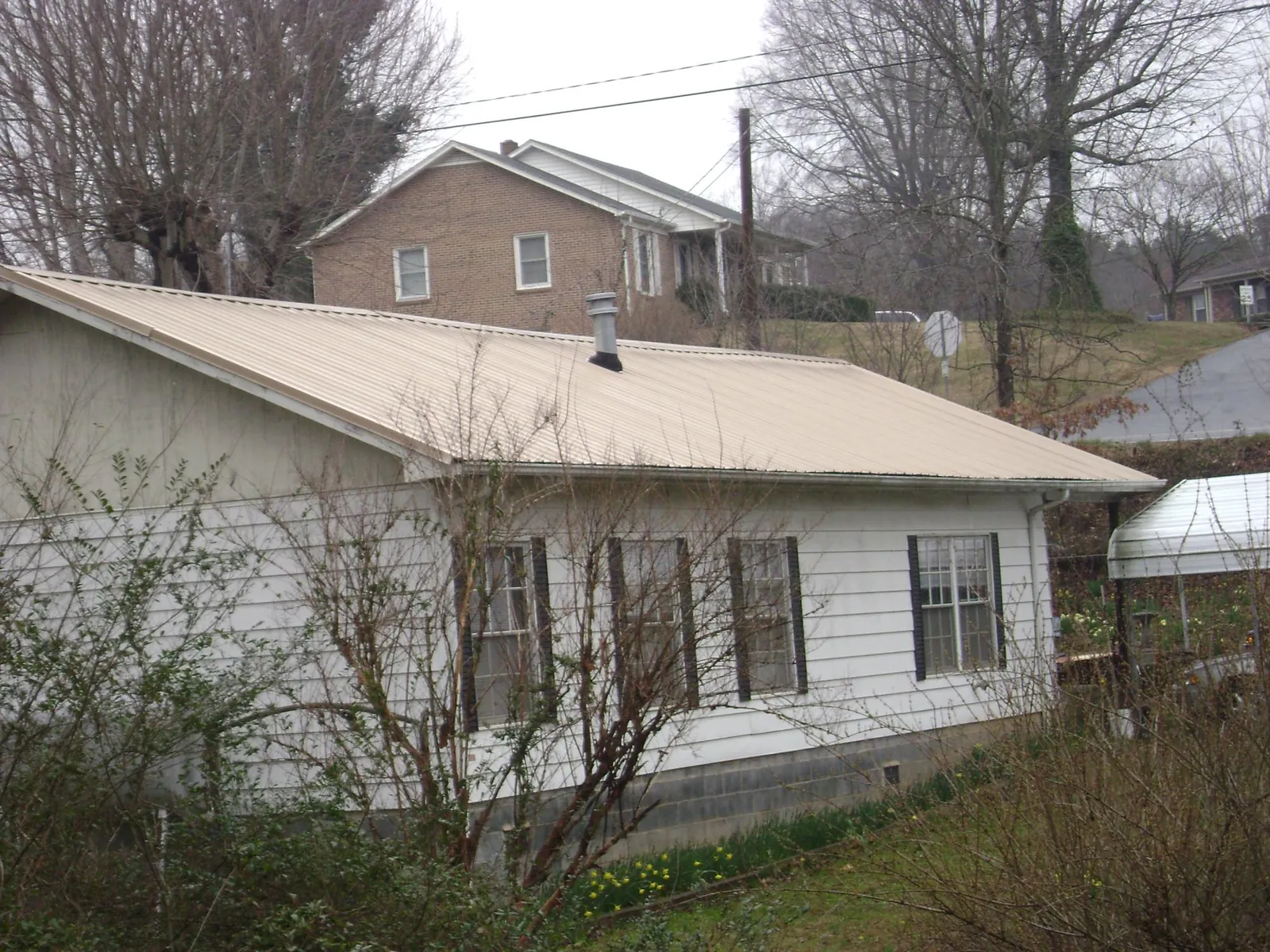 Tan metal roof on a white sided house set into a hillside — Commercial Roofing by Roofing Brothers in Tracy City
